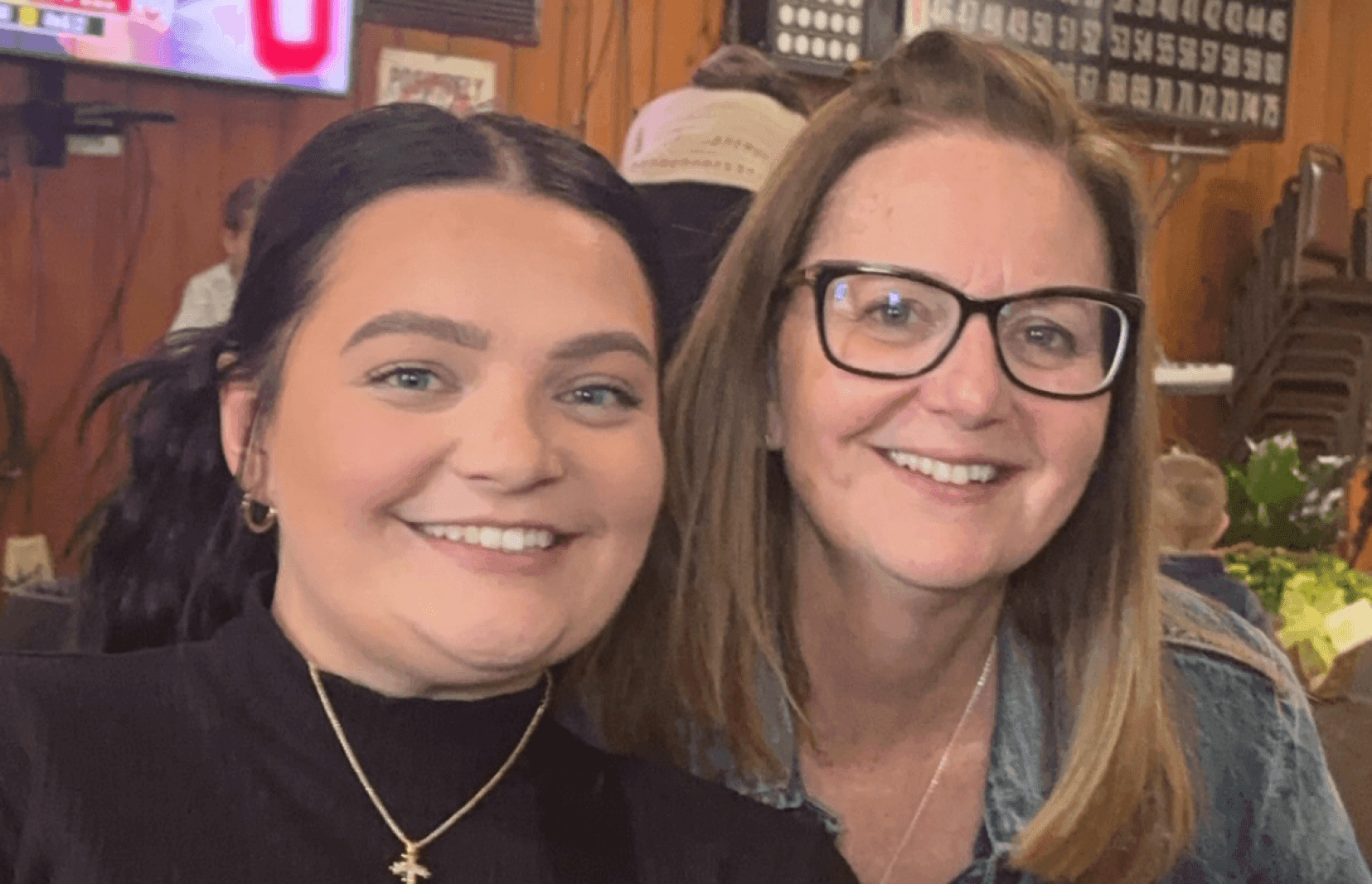 Joy, who has light brown hair and glasses, sitting next to her daughter with dark brown hair. 