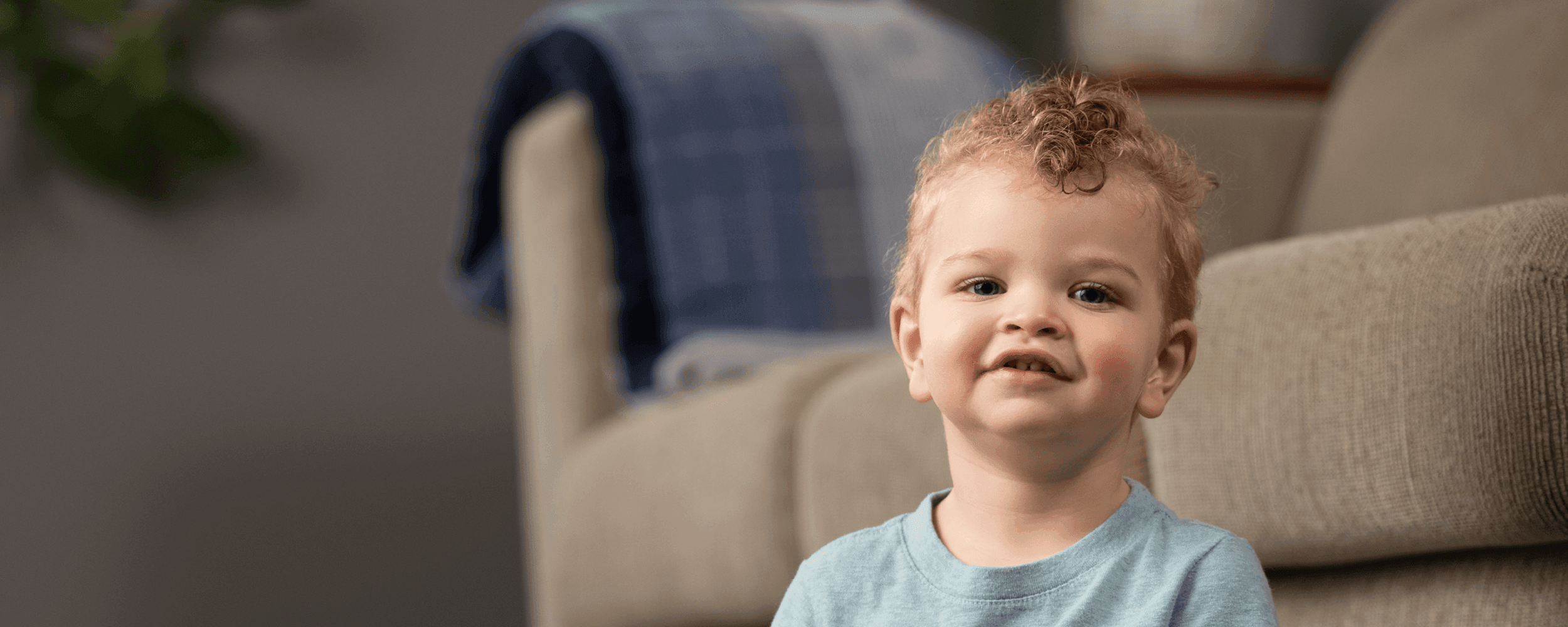 Toddler boy with light curly hair sitting on the ground in a living room