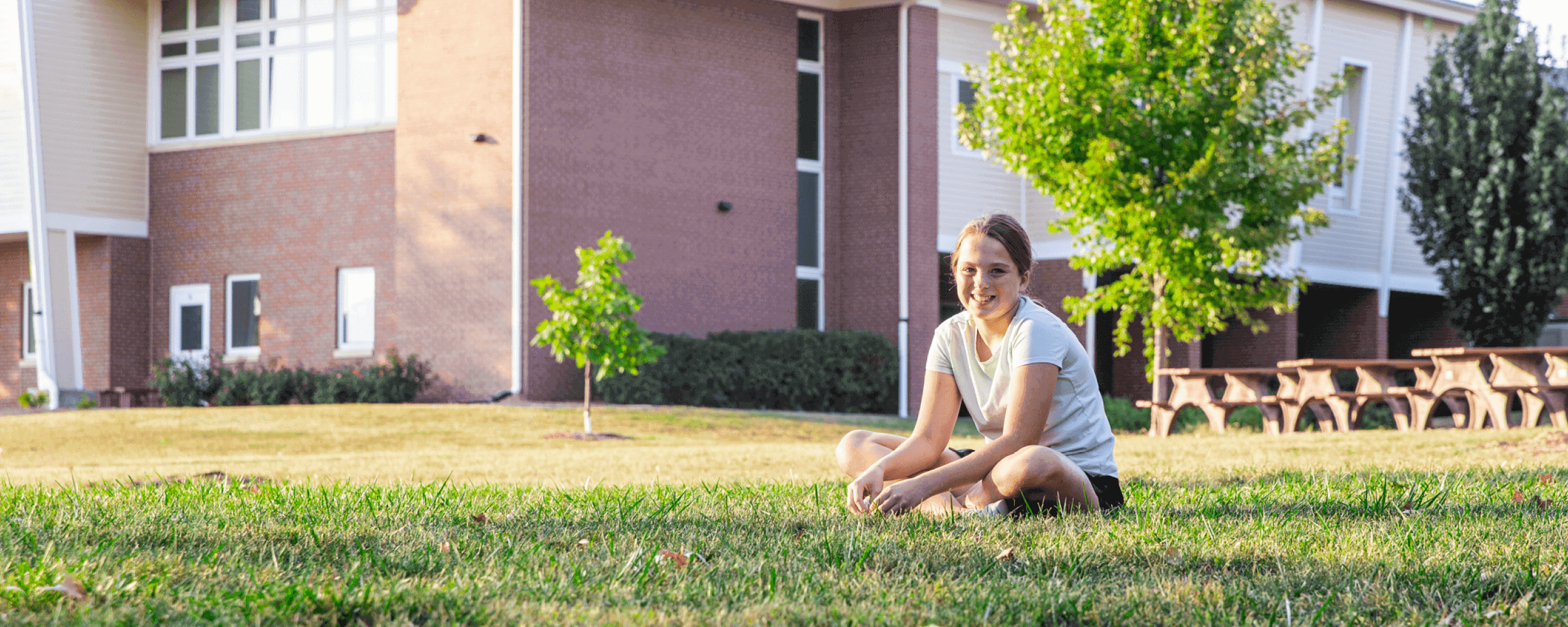 Young teen girl sitting in the grass in CEDARS backyard